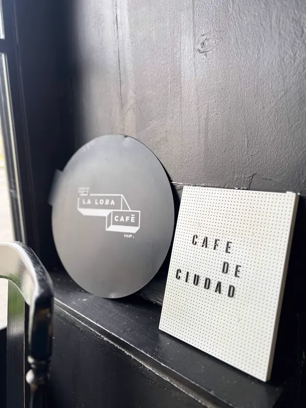 Tapa negra con el logo de La Loba Café y un letrero de letras blancas que dice Café de ciudad