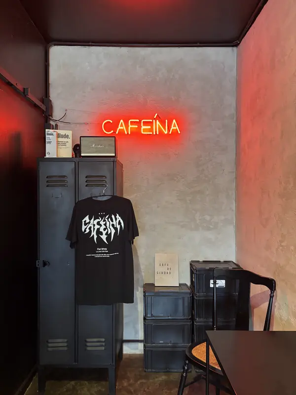 Rincón del local con un neón rojo que dice Cafeína, un locker metálico y una polera colgada