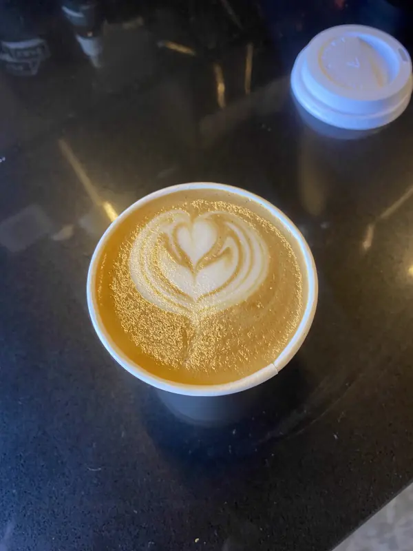 Latte en vaso de papel con un corazón dibujado en la espuma