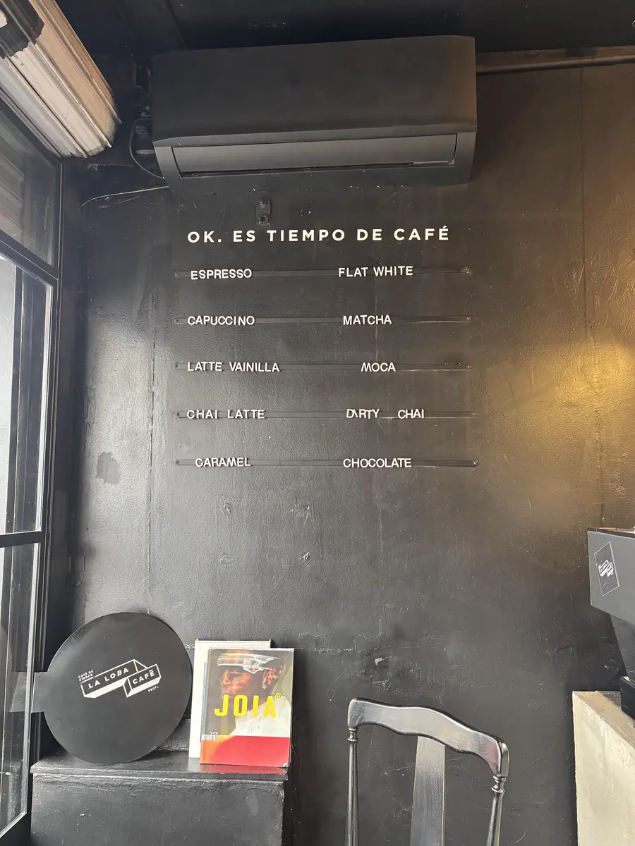 La pared negra del local con la carta en letras blancas bajo el título OK. Es tiempo de café, una silla y la tapa con el logo