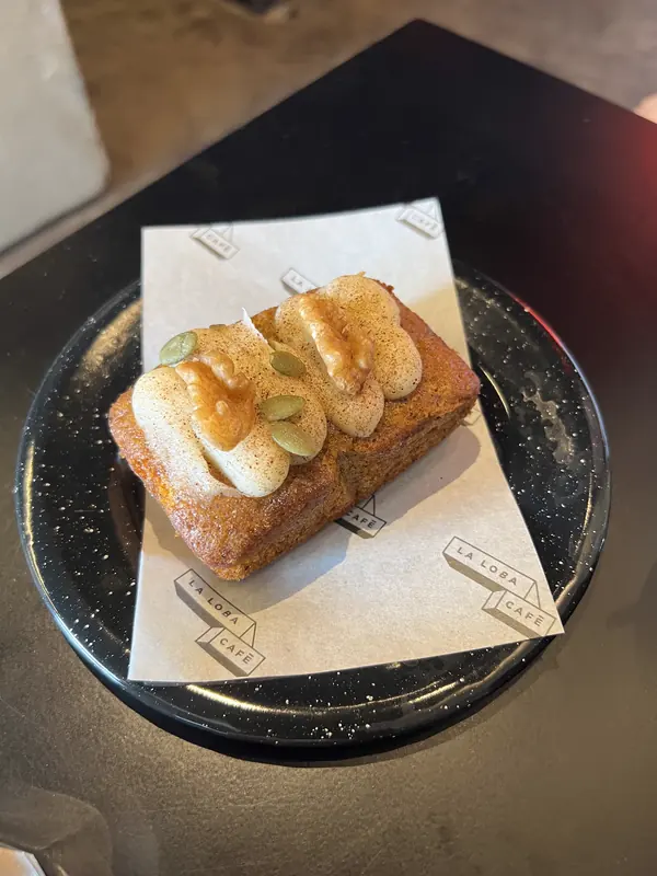 Queque con crema y semillas sobre un plato negro, con el papel de La Loba Café