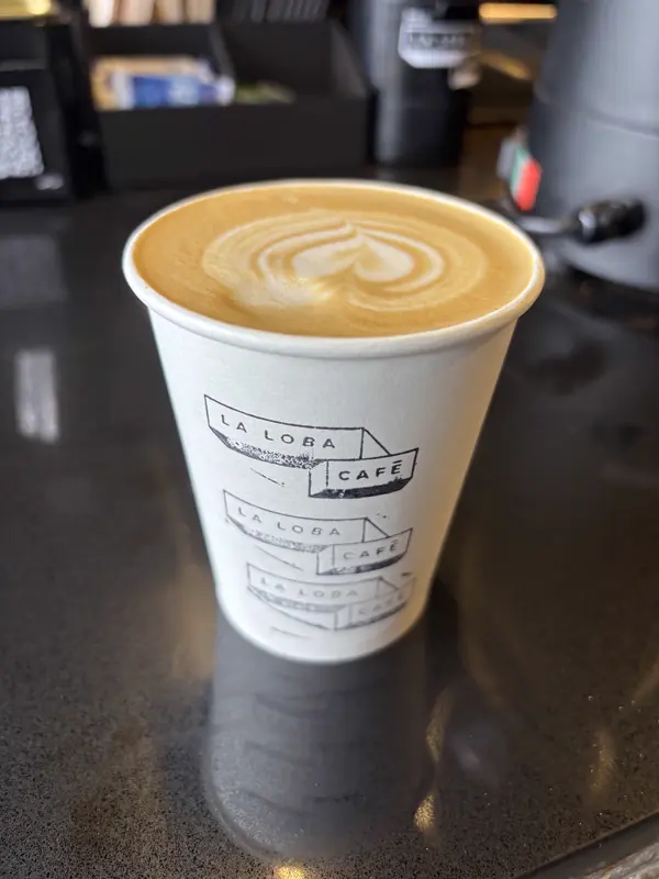 Vaso para llevar de La Loba Café con latte, sobre la barra